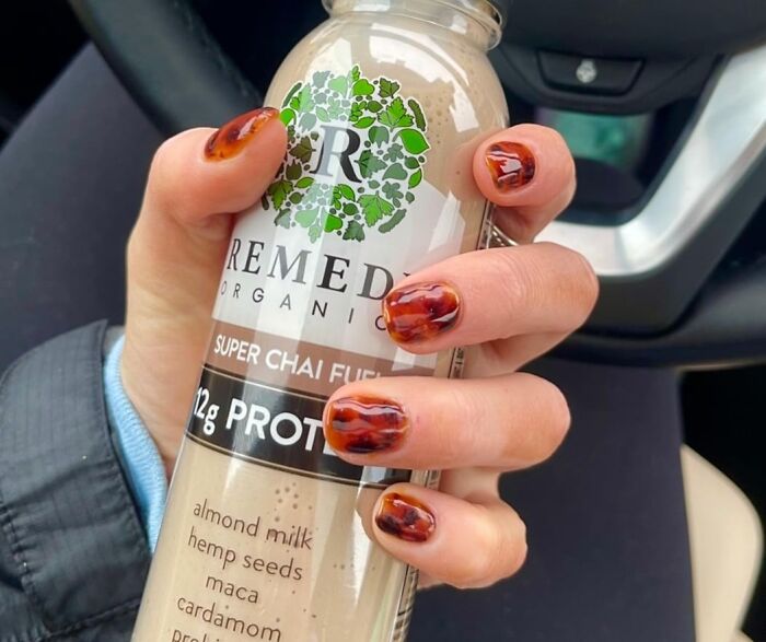 Hand with stylish nails holding a Remedy Organics chai drink in a car.