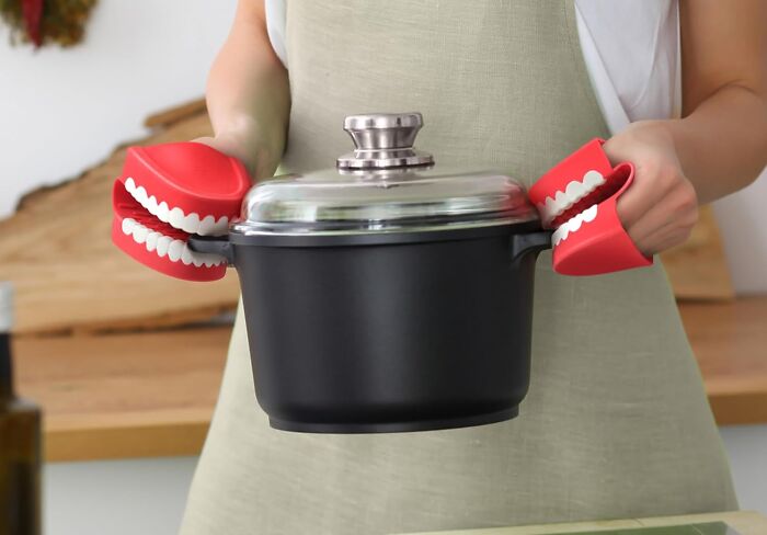 Person using novelty pot holders shaped like teeth to hold a cooking pot.