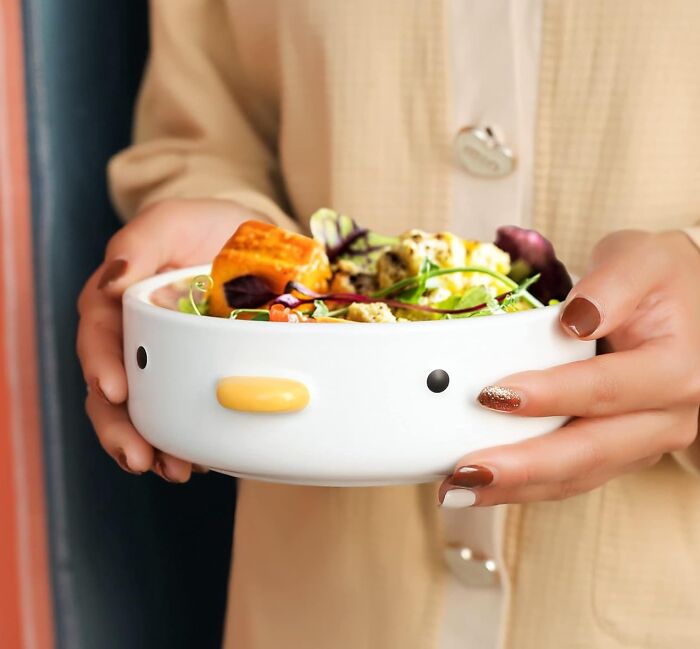 Hands holding a playful bowl featuring a cartoon face, filled with a vibrant salad; ideal for showcasing cool products.