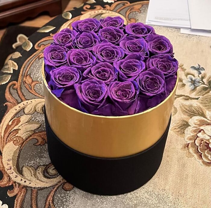 Purple roses arranged in a gold and black round box, perfect for Valentine's Day gifting.