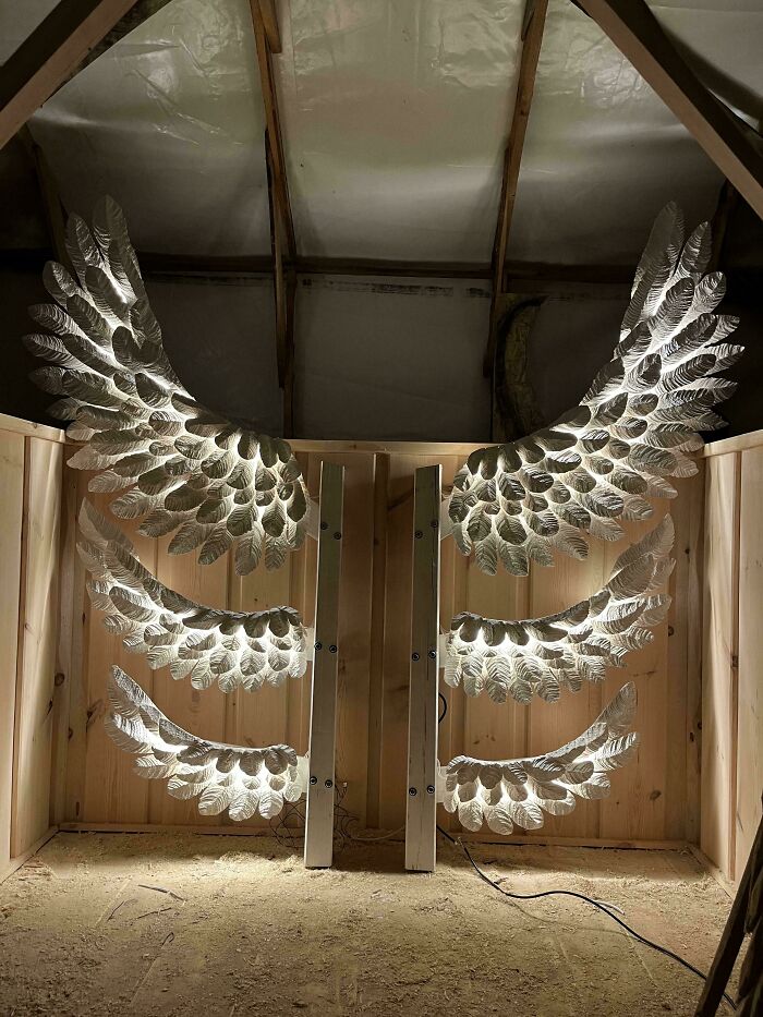 Woodworking project featuring illuminated wooden wings mounted on a rustic backdrop, showcasing intricate craftsmanship.