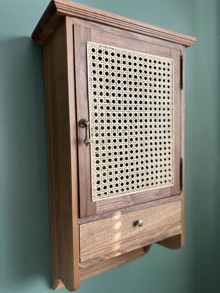 Woodworking project: handcrafted wooden cabinet with woven door panel, mounted on a green wall.