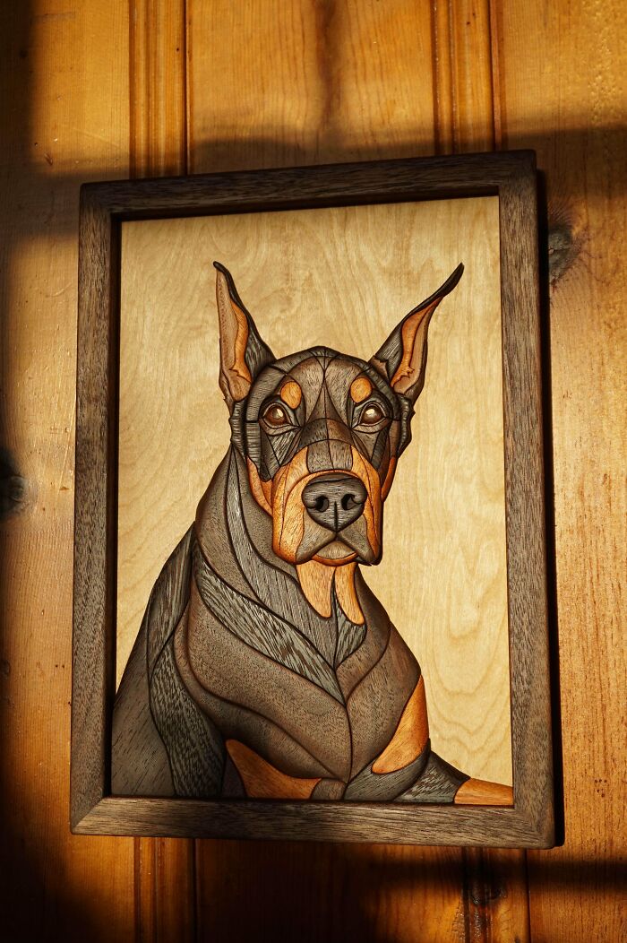 Woodworking project of a Doberman portrait in a wooden frame against a wooden wall.