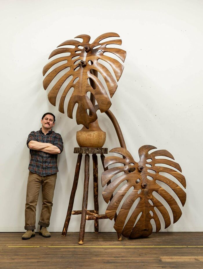 Man standing next to impressive woodworking project featuring large wooden sculptures of Monstera leaves.