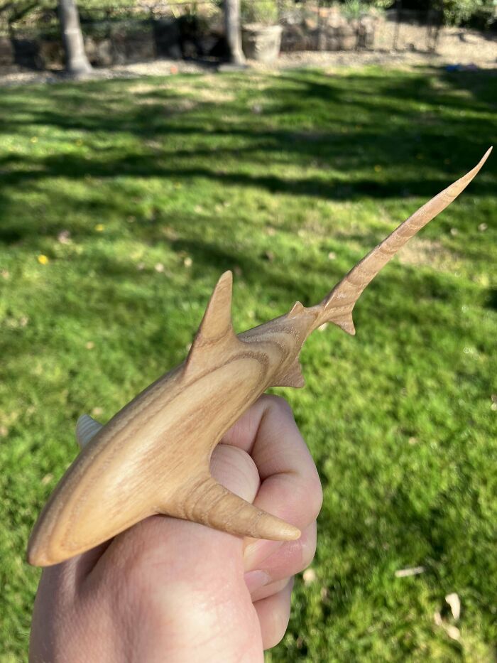 Hand holding a detailed wooden shark carving, showcasing impressive woodworking craftsmanship.