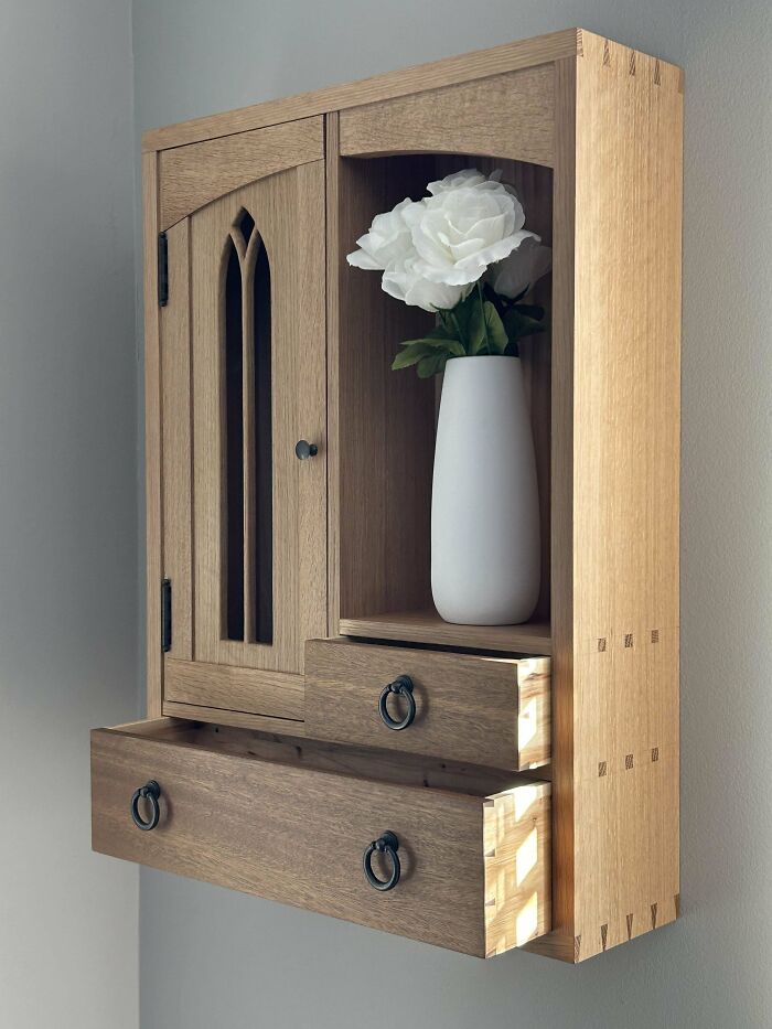 Woodworking project showcasing a wall-mounted wooden cabinet with drawers and a decorative vase with white flowers.