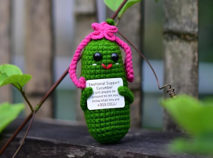 Cute crocheted cucumber with a pink hat and a humorous sign adding fun to office supplies.