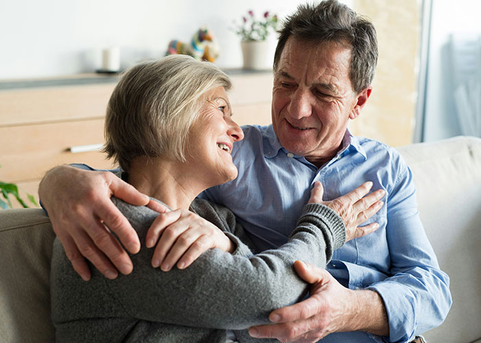 A happy couple sitting on a couch, embracing and smiling, discussing financial income combination.