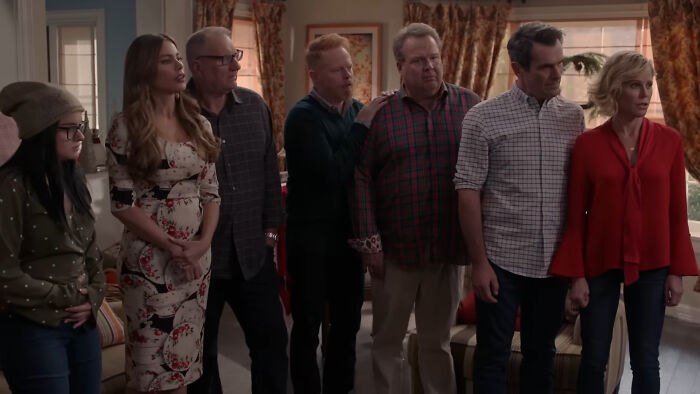 Cast of a beloved comedy show standing together in a living room setting.