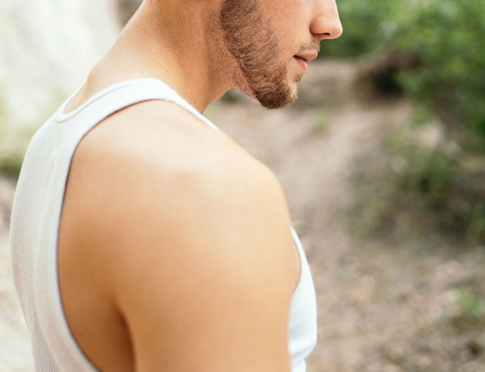 A man in a white tank top, outdoors, symbolizing family secrets and untold stories.