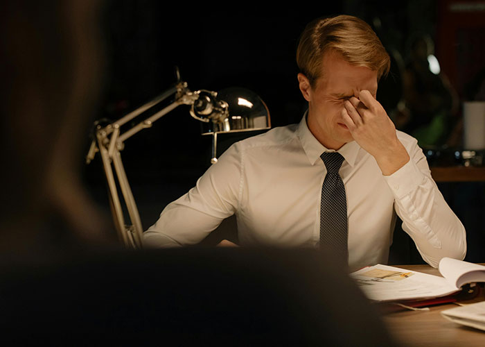 A man in a shirt and tie sitting at a desk, looking stressed after an awkward job interview.