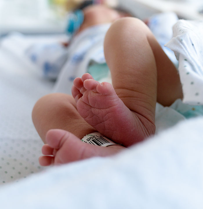 Newborn baby lying in a NICU bed with an identification band visible.