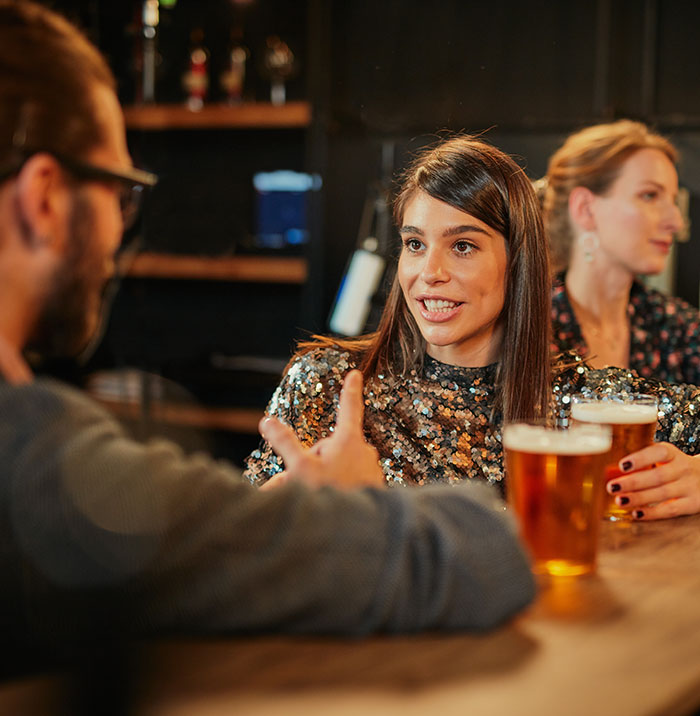 Woman on date at a bar, holding a beer, conversing with a man in a casual setting.