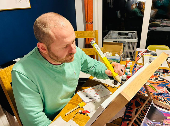 Man painting on canvas in a well-lit room, surrounded by art supplies, focusing on his work.