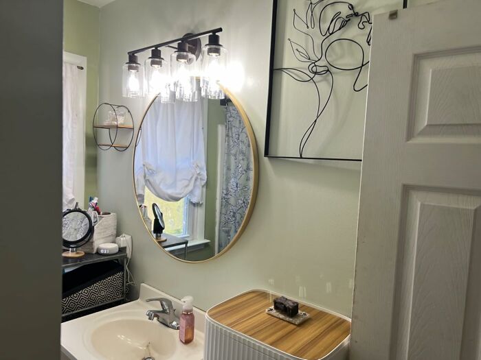 Modern bathroom with round mirror, stylish light fixture, and new products on counter.