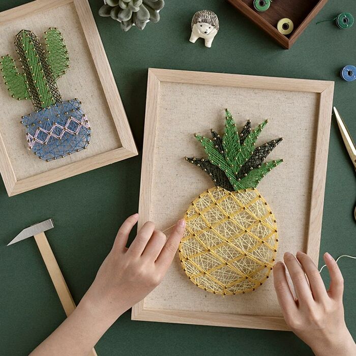 Hands creating string art of a pineapple and cactus, showcasing new hobbies 2025.