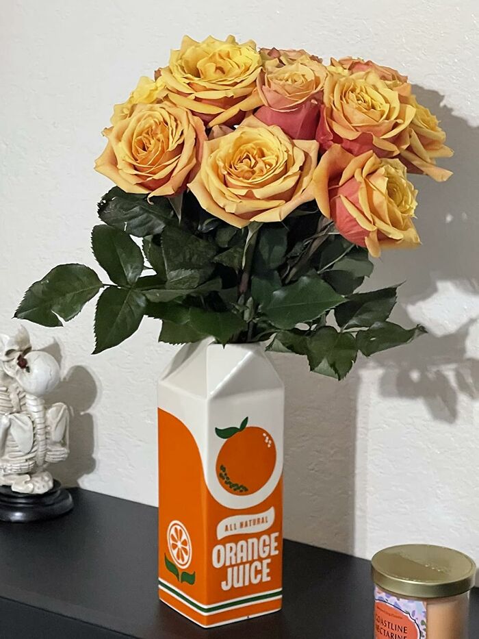 Retro Fever: Yellow roses in a vintage orange juice carton vase on a black shelf.