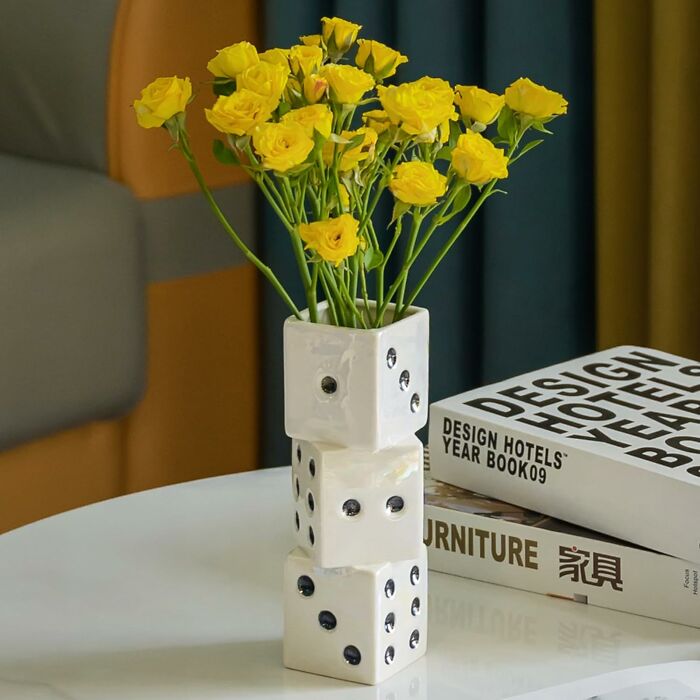 Yellow flowers in a retro dice vase on a white table, with design books in the background.