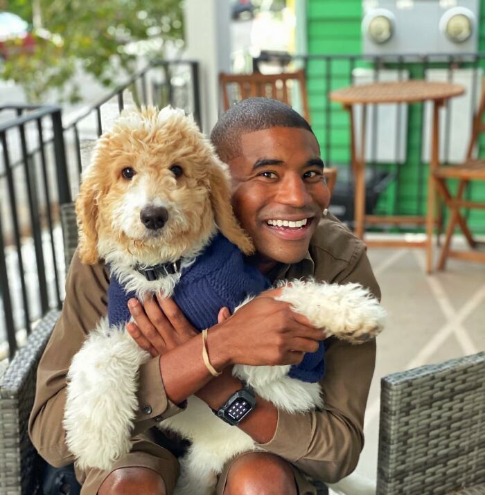 UPS driver smiling with an adorable dog in a sweater on his delivery route.