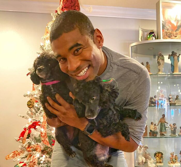 UPS driver smiling and holding two adorable poodles, a festive tree in the background.