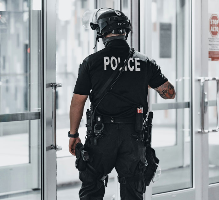 Police officer in tactical gear standing near a glass door, highlighting law enforcement activities.