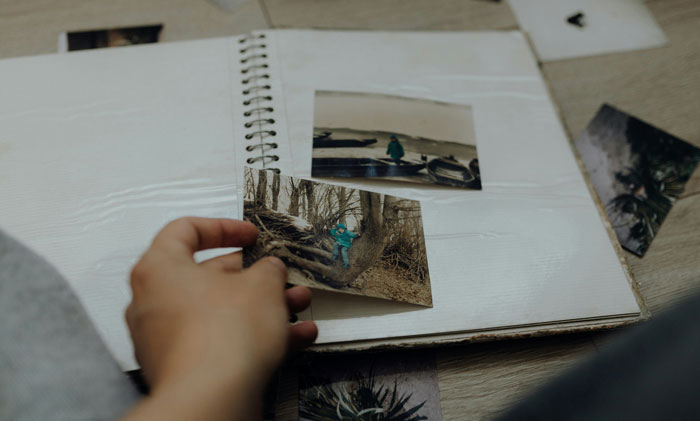 Hand holding a family photo album, with scattered photos, representing untold family stories.