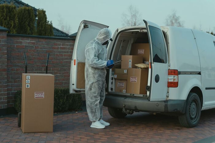 Person in protective suit loading labeled boxes into a van, concept of unethical life hack.