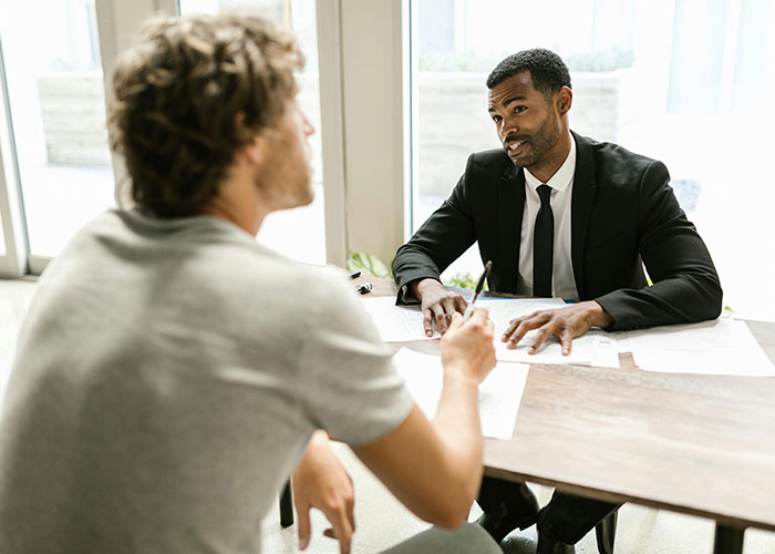 Two men in a job interview, one in a suit, discussing at a table, highlighting awkward job interview moments.