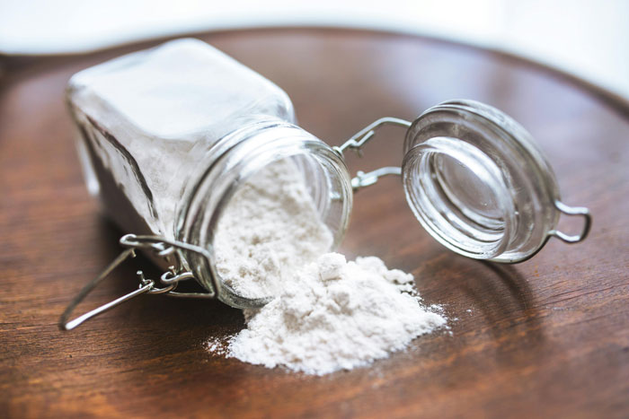 Open glass jar spilling white powder on wooden surface, showcasing quality life hack storage tip.