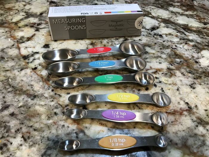 Set of colorful measuring spoons on a marble countertop, essential for getting better at cooking.