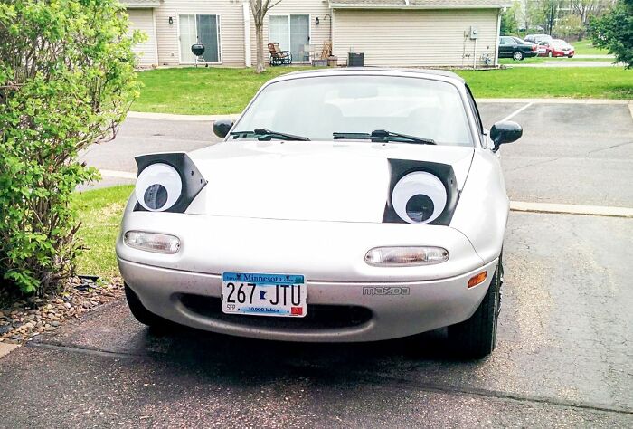 Car with googly eyes on headlights, showcasing quirky gems that add fun and functionality in a suburban driveway.