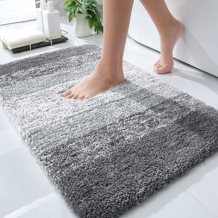 Bare feet stepping on a cozy, gray gradient bath mat in a bright bathroom setting.