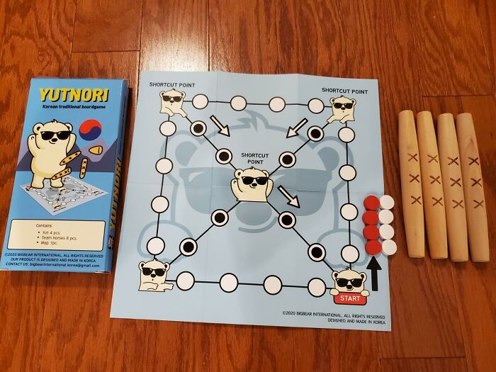 Board game setup similar to Squid Games, featuring a Yutnori game board with sticks and tokens on a wooden floor.