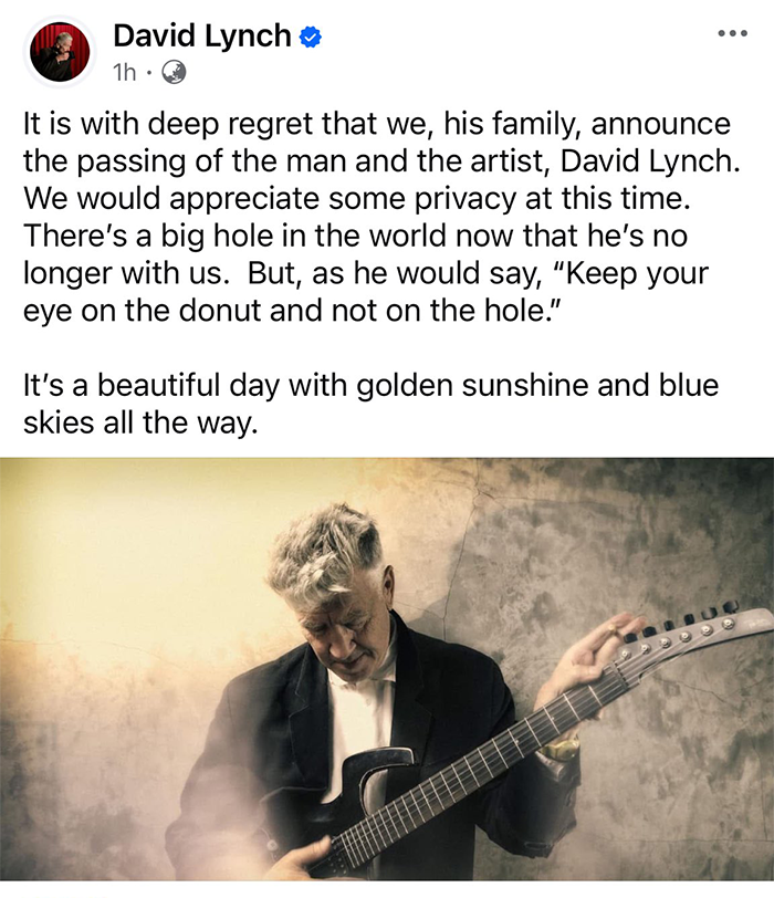 David Lynch, director, holding a guitar against a textured wall, reflecting somberly.