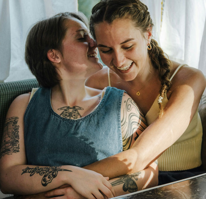 Two people with tattoos sharing a lighthearted moment on a sunny day, symbolizing unspoken family stories.