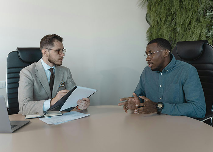 Two men in a professional setting during a job interview, discussing awkward interview experiences.