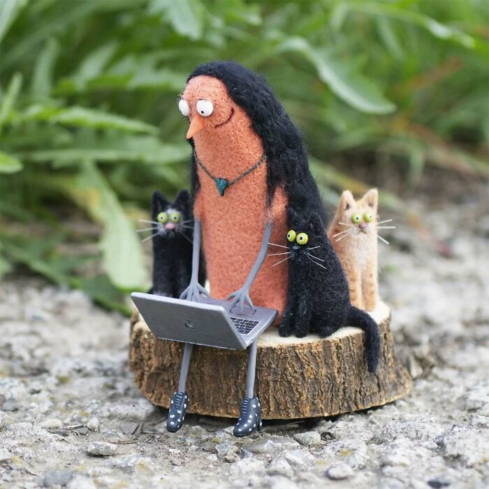 Strange art doll of a person with cats, sitting on wood, using a laptop, created by a Georgian artist.