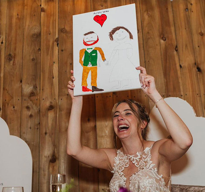 Woman joyfully holding a viral painting of herself and husband, featuring simple drawings with a heart above.