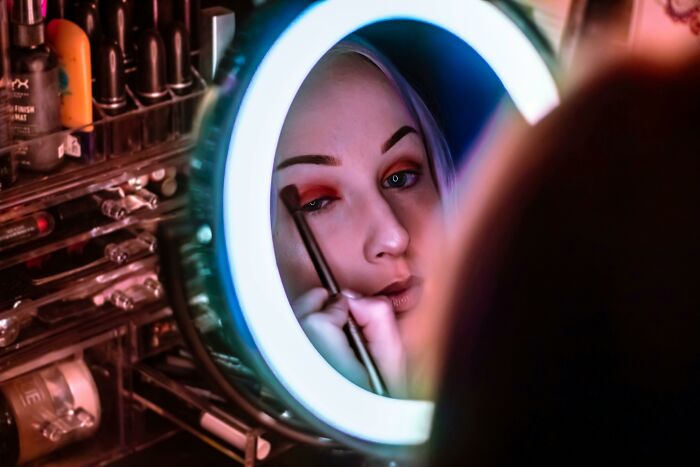 A person applying makeup, reflected in a circular mirror, with cosmetics organized around.