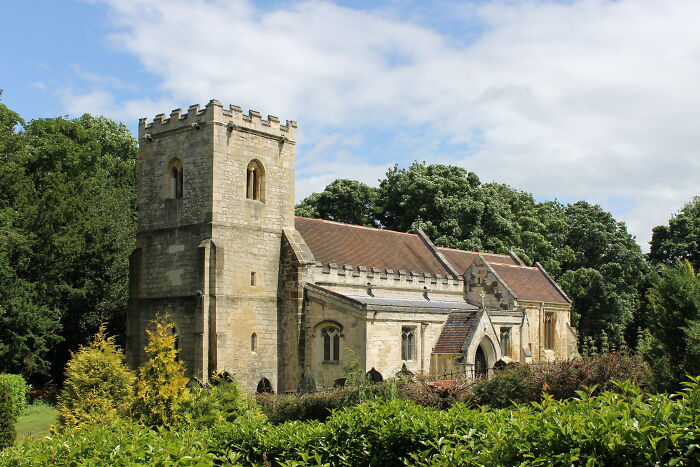 Historic stone church surrounded by lush greenery under a cloudy sky, showcasing fascinating architecture details.