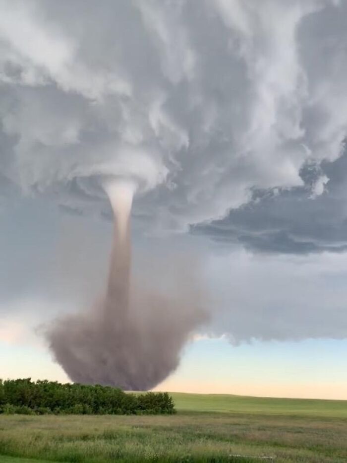 A dramatic tornado under a stormy sky in open fields, showcasing incredible world photos of natural phenomena.