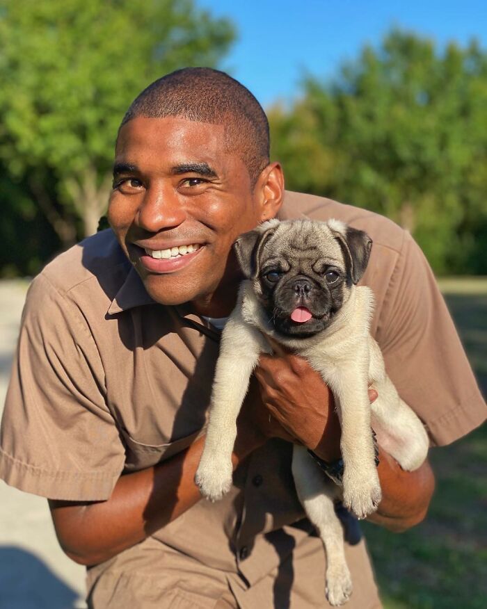 UPS driver smiling and holding an adorable pug outdoors during delivery route.