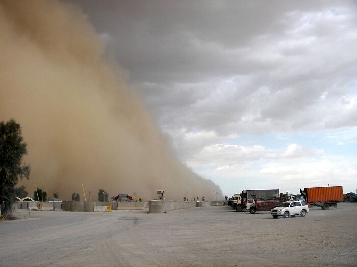 Dust storm looming over vehicles on a road, showcasing stunning natural phenomena.