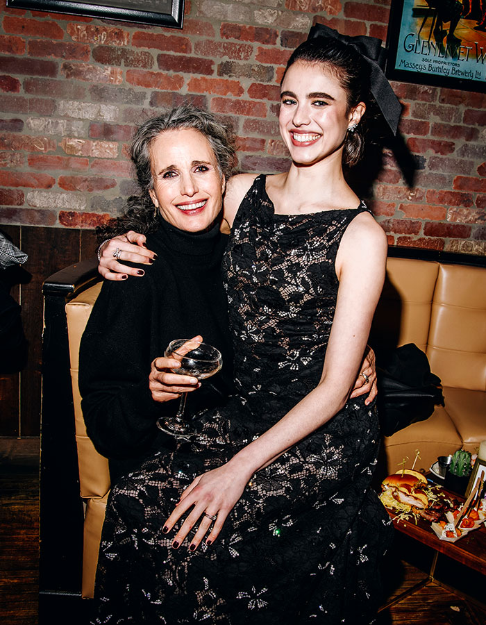 Margaret Qualley sitting on her mom's lap, both smiling at a social event, highlighting reverse nepotism.