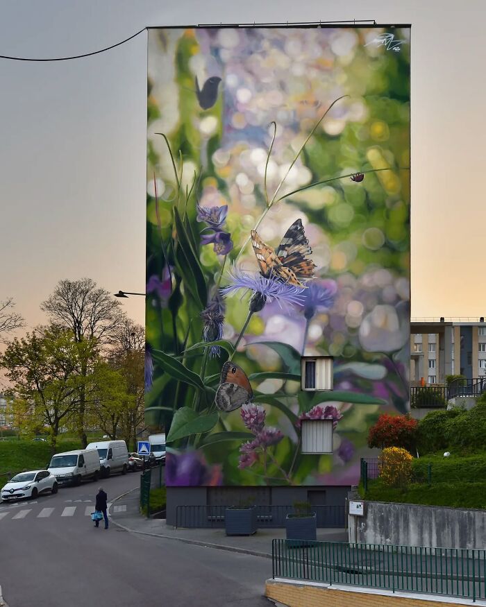 Hyper-realistic mural of butterflies and flowers painted on a tall building by a French artist.