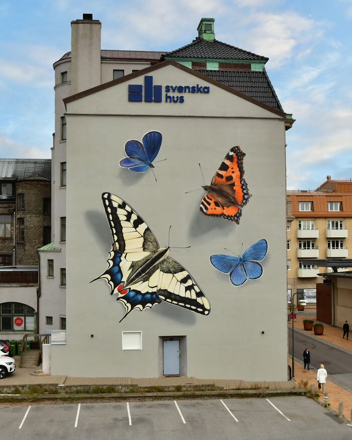 Hyper-realistic butterfly murals on a building wall by a French artist, showcasing stunning detail and color.