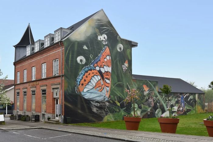 Hyper-realistic mural of a butterfly on a building wall by French artist, featuring vivid colors and detailed greenery.