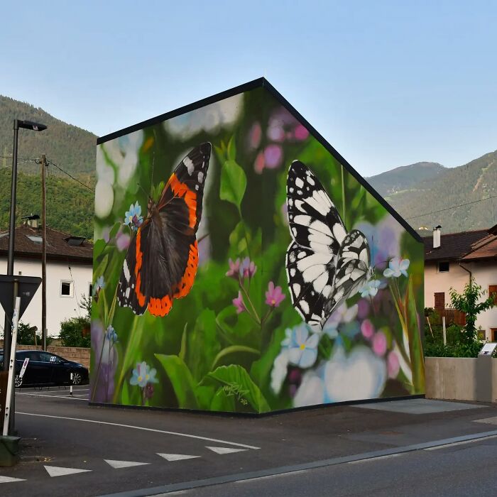 Hyper-realistic butterfly murals painted on a building by a French artist, featuring vibrant greenery and flowers.