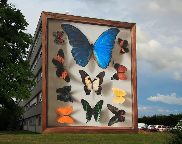 Hyper-realistic butterfly mural on a building by a French artist, featuring various colorful butterfly species.