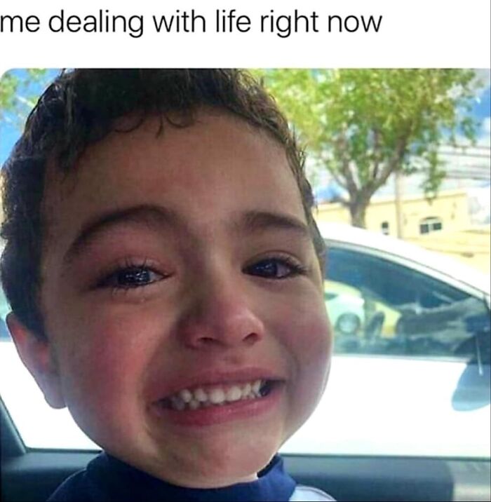 Young child making a strained smile while crying, sitting in a car, capturing an introverted feeling.